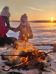 Une famille avec enfant mange au coin du feu en Laponie au couché du soleil